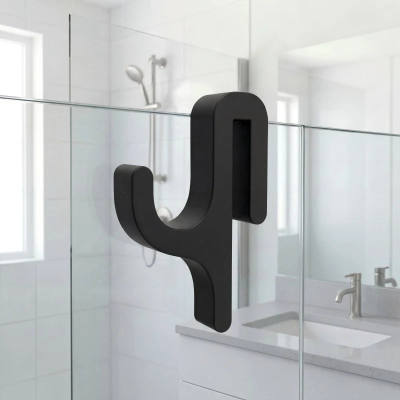 A black, modern Y-shaped shower door towel hook mounted on a glass panel in a bathroom setting.