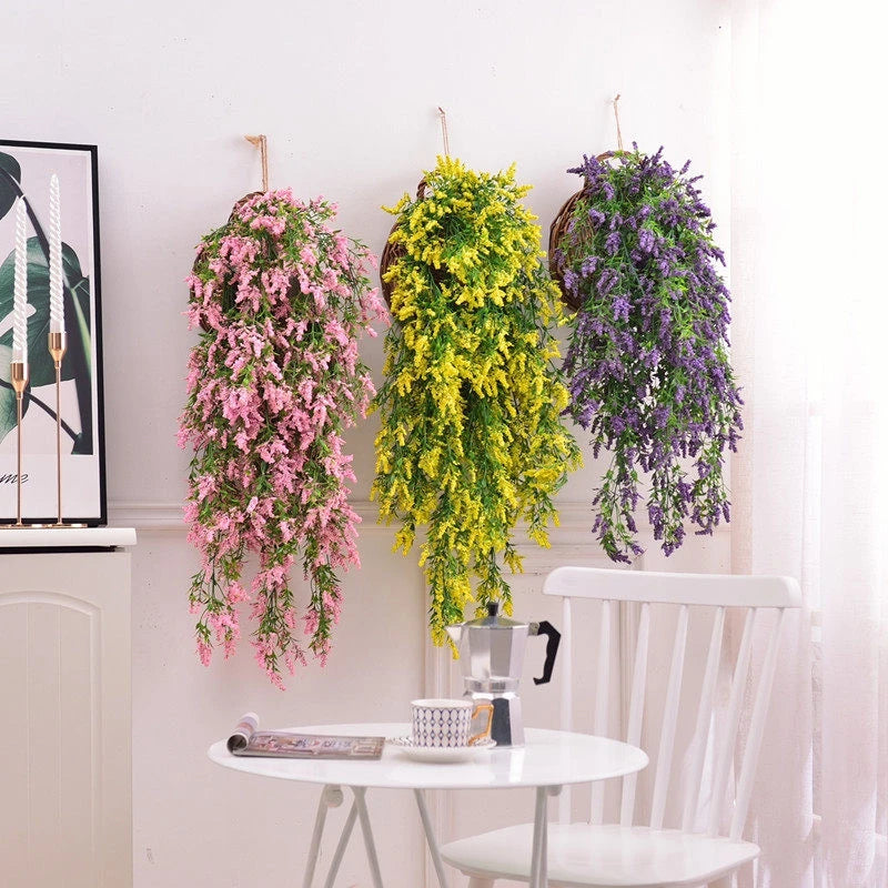 Three hanging silk morning glory vine flowers in pink, yellow-green, and purple on a white wall.