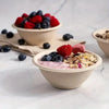 A serving of mixed berries and nut crumble in a disposable paper bowl, set against a white marble background.