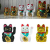 A collection of electric waving lucky cat figurines in gold and white, depicting cats for good fortune.