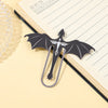 A black metal bookmark shaped like a four-winged dragon resting on a yellow lined notebook.