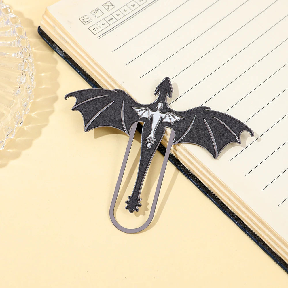 A black metal bookmark shaped like a four-winged dragon resting on a yellow lined notebook.