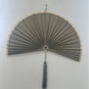 Handwoven bamboo wall fan decor with a light gray fan and tassel mounted on a white wall.