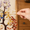 A hand is placing small crystal ornaments onto a branch of a decorative, bendable tree ornament.