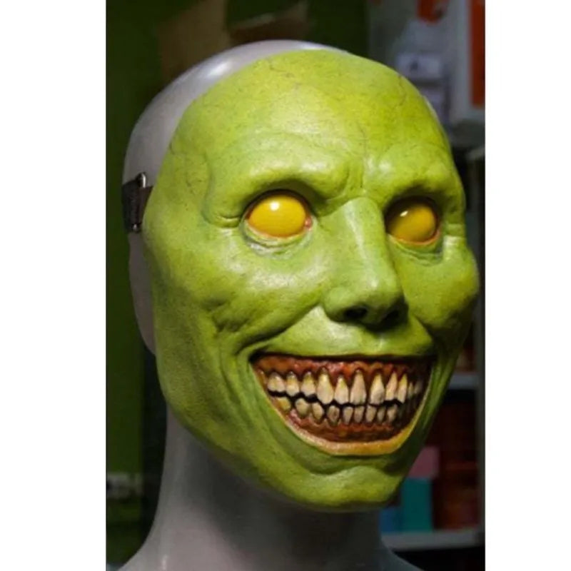 A green latex mask resembling a grotesque face with yellow eyes and a stitched mouth, displayed on a mannequin head.