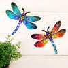 A vibrant, iridescent dragonfly sculpture with blue and purple wings is displayed on a white wooden surface.