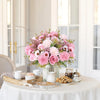 A pink and purple artificial silk rose and daisy bouquet displayed on a white table with tea service items.