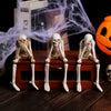 Three resin skeleton skull figurines seated on a wooden box with a white cobweb in the background.