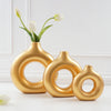 A golden resin vase shaped like interlocking rings holds white tulips on a white surface.