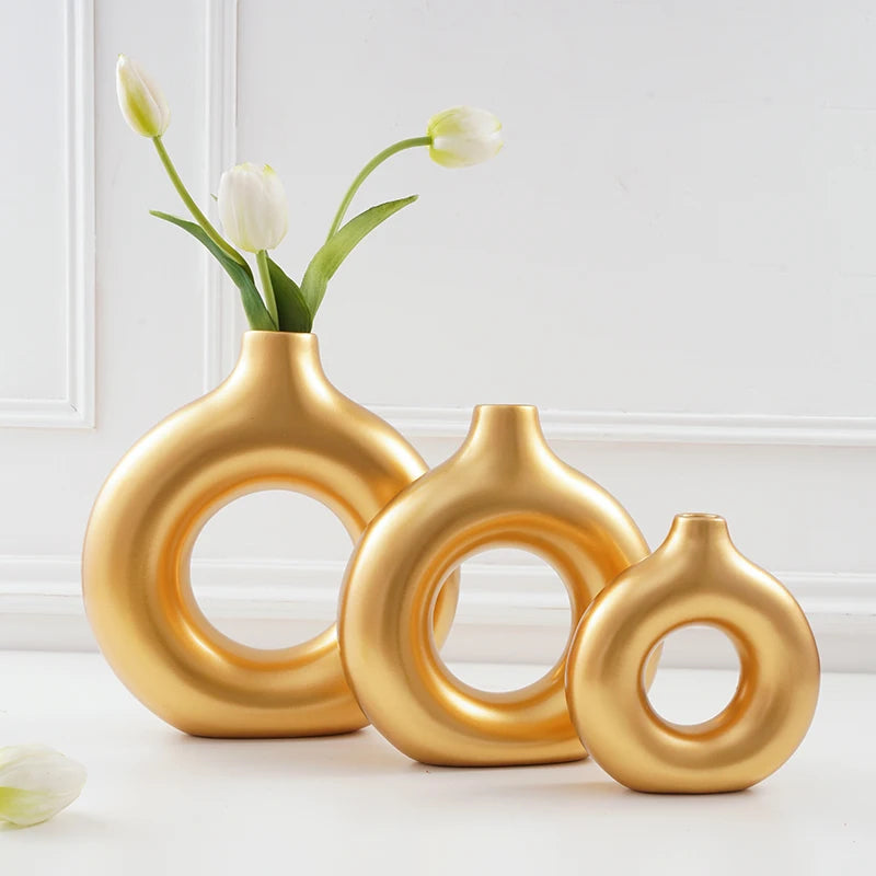 A golden resin vase shaped like interlocking rings holds white tulips on a white surface.