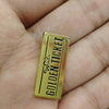 A gold-colored enamel lapel pin shaped like a ticket with the text GOLDEN TICKET on it.