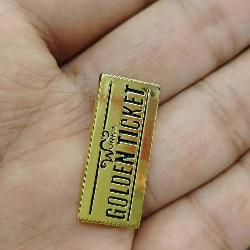 A gold-colored enamel lapel pin shaped like a ticket with the text GOLDEN TICKET on it.