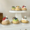 A display of six miniature cupcakes with various toppings arranged on white stands.