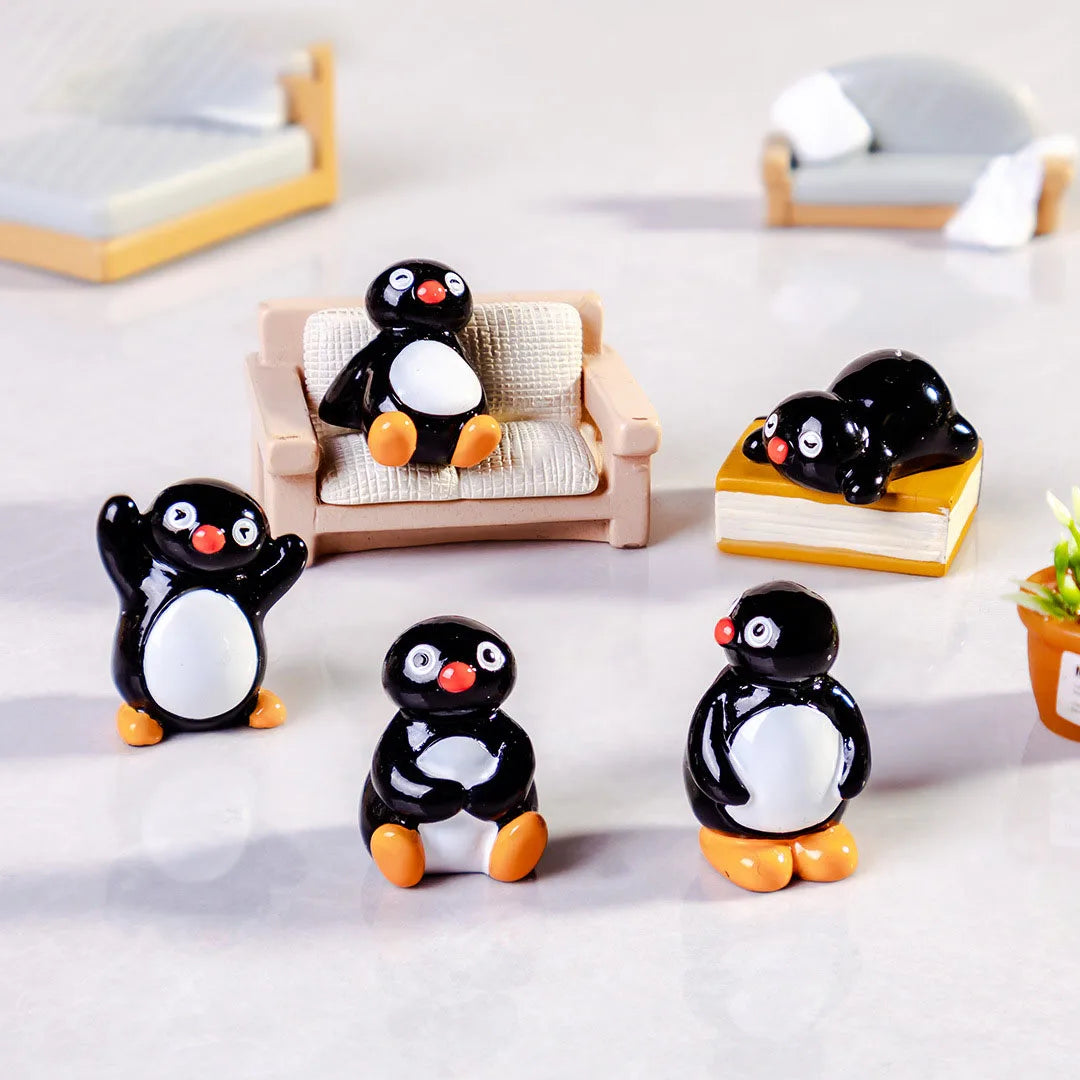 A collection of cute cartoon penguin resin figurines in black and white with orange accents displayed on a white surface.