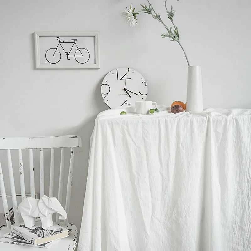 A white classic cotton rectangle tablecloth is displayed on a table, set with a white cup and fruit.