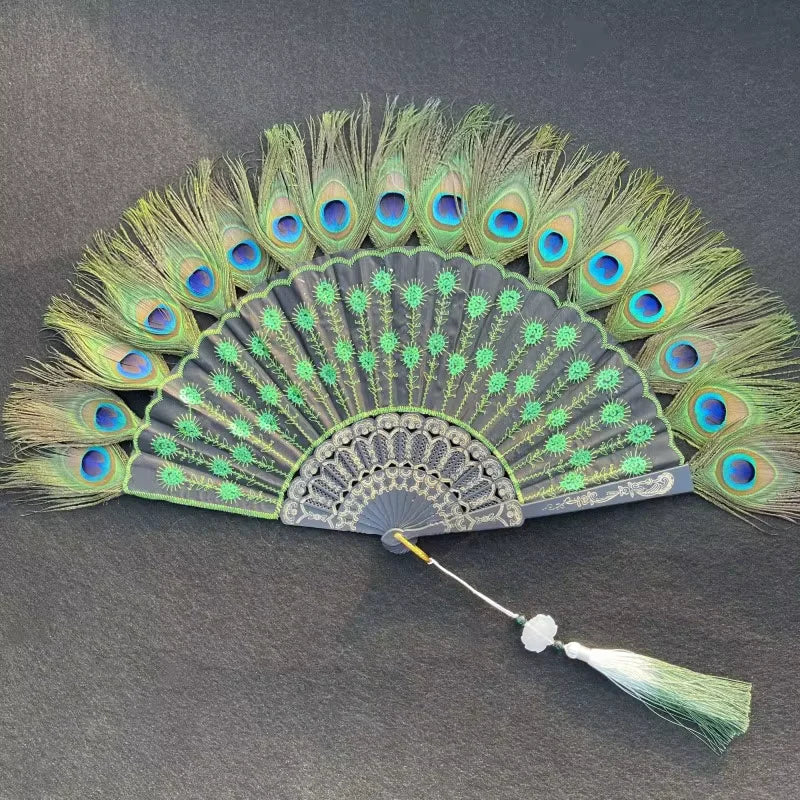 Un éventail à main en plume de paon naturel avec des plumes vertes et bleues, exposé sur un fond sombre.