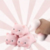 A hand is holding several adorable pink pig mochi squishy stress relief toys against a light pink striped background.
