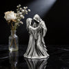 A silver-toned sculpture of a couple embracing, resembling a Gothic Grim Reaper theme, displayed on a dark surface.