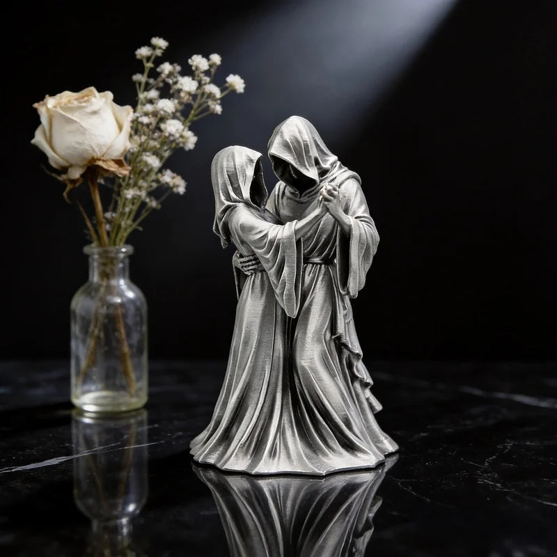 A silver-toned sculpture of a couple embracing, resembling a Gothic Grim Reaper theme, displayed on a dark surface.