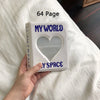A white photo album titled My World and My Space is held in a hand on a white bedsheet.