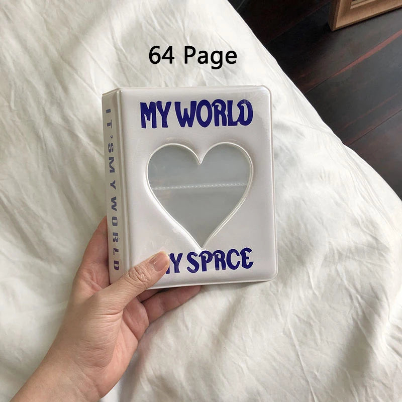A white photo album titled My World and My Space is held in a hand on a white bedsheet.