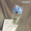 A clear plastic bag containing a handmade blue crochet tulip bouquet with the word LOVE written on the stem.