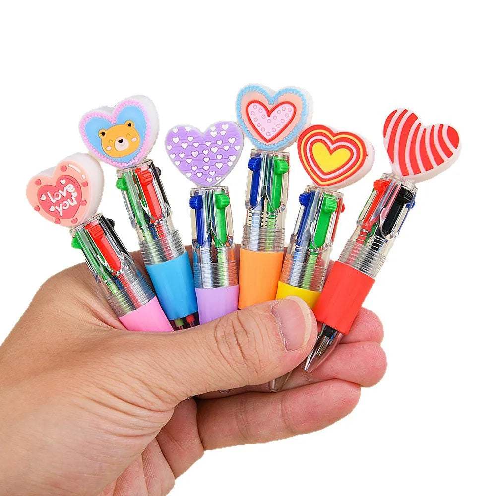 A hand holds a set of four heart-shaped multicolor ballpoint pens with various colored bodies and decorative tips.