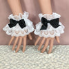 White ruffled lace wrist cuffs with black bowknot accents displayed on a mannequin hand.