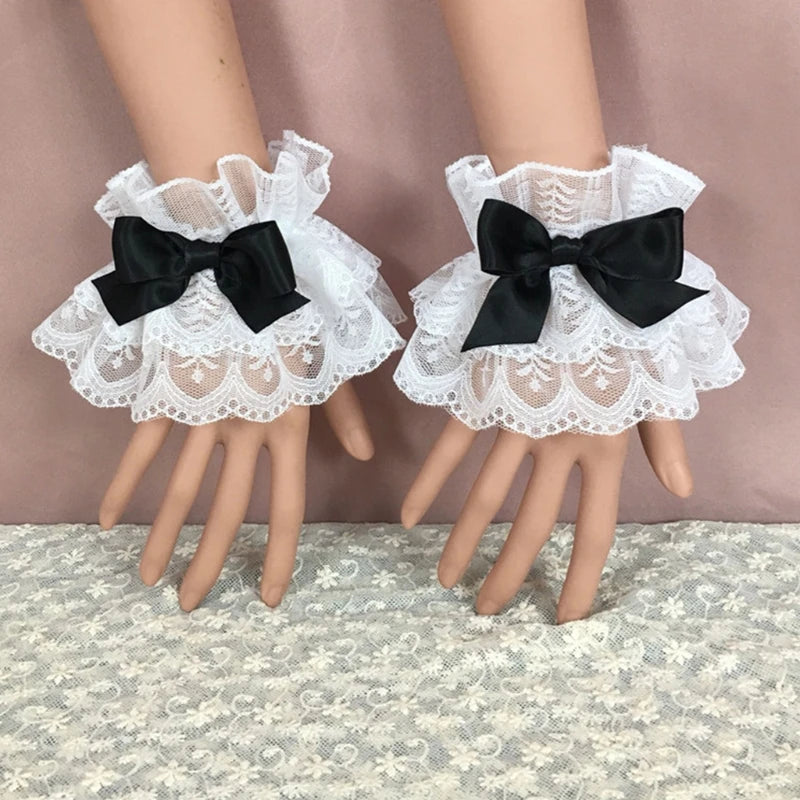 White ruffled lace wrist cuffs with black bowknot accents displayed on a mannequin hand.