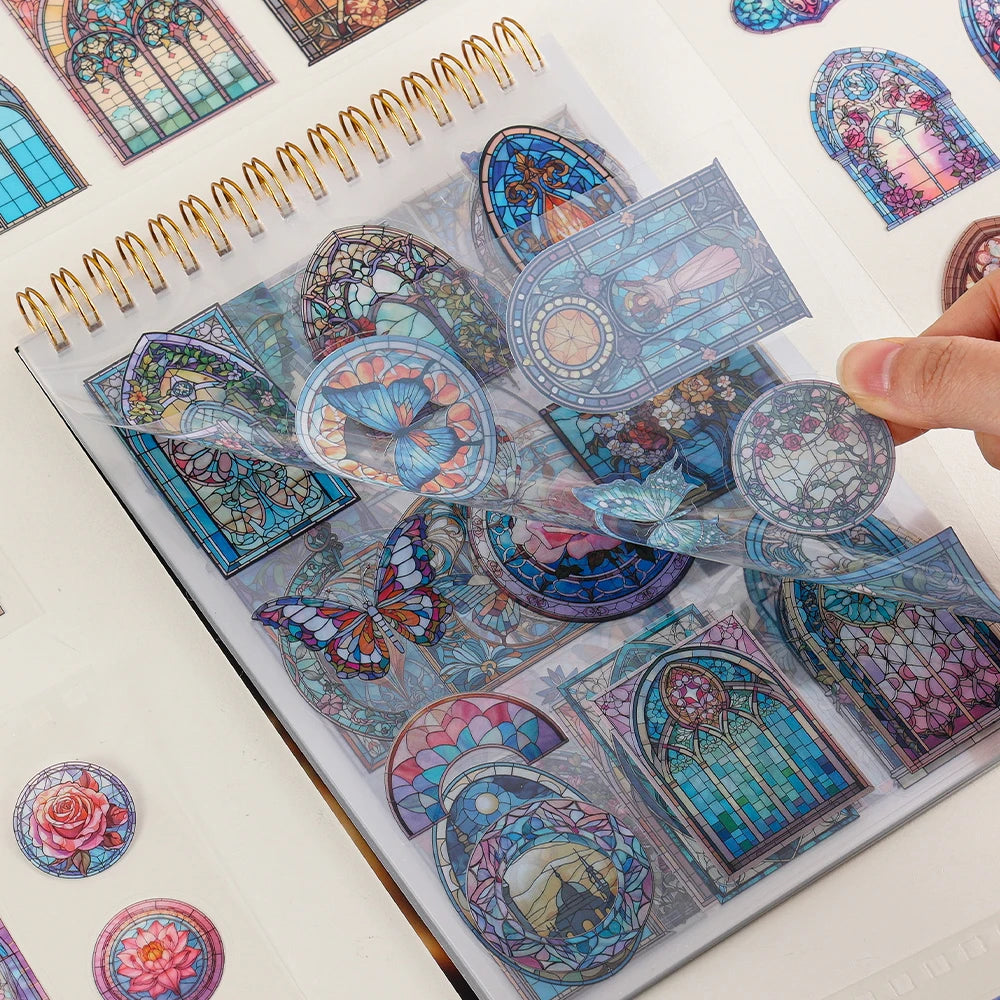 A hand is placing vintage floral window scrapbooking stickers into a spiral-bound notebook.