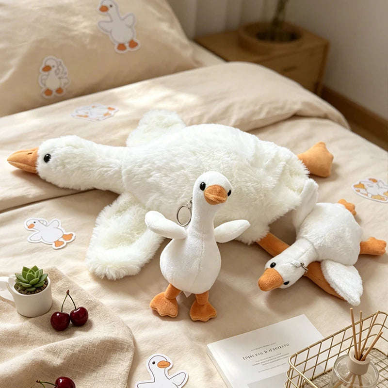 A white duck plush toy is shown lying on a beige fabric, with small decorative items nearby.