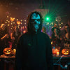 A person wearing a dark hoodie with a realistic skull mask for Halloween in a dimly lit party setting.