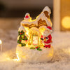 A glowing Christmas gingerbread house ornament made of resin with festive decorations set in snow.
