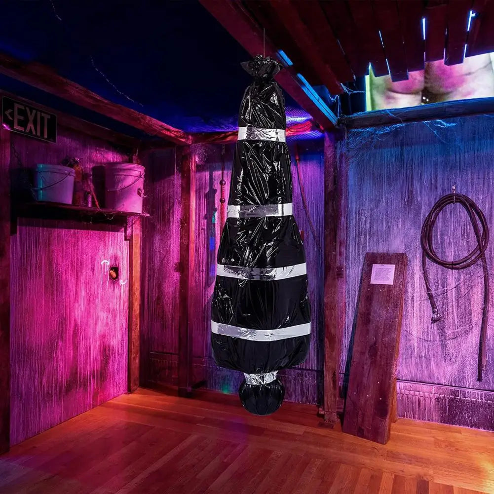 A realistic dead victim prop draped in black plastic and white stripes displayed in a dimly lit room.