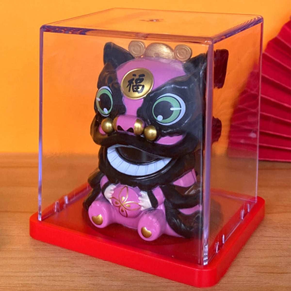 A solar-powered waving lucky cat figurine with black and pink features displayed in a clear box on a red stand.
