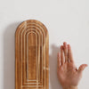 Jarrón de pared arqueado de madera con ranuras verticales montado en una pared blanca.