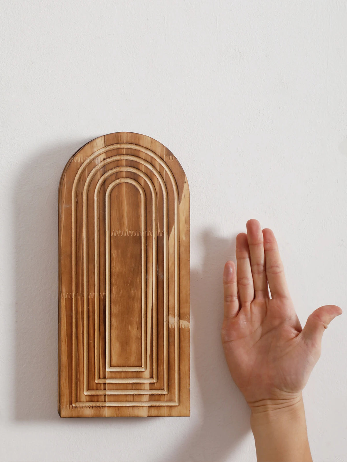 Jarrón de pared arqueado de madera con ranuras verticales montado en una pared blanca.