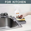 A hand is using a silicone faucet splash guard and drying mat to clean a kitchen sink.