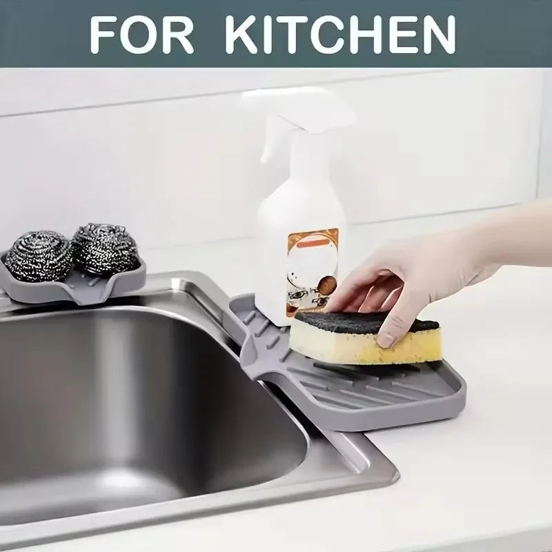 A hand is using a silicone faucet splash guard and drying mat to clean a kitchen sink.