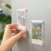 A hand holds a magnetic mini photo frame featuring a picture of a pink and red object.