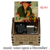 A hand-cranked wooden music box featuring an illustration of a woman and a man, with the title Once Upon a December.