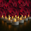 A close-up of glowing LED tea light candles set on a dark wooden surface, surrounded by red roses.