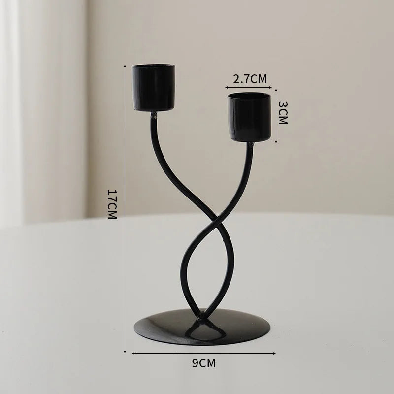 A black iron candle holder with a curved stand and two cylindrical candle holders.