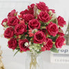 A bouquet of deep red silk artificial roses with green foliage and small pink accents in a clear glass vase.