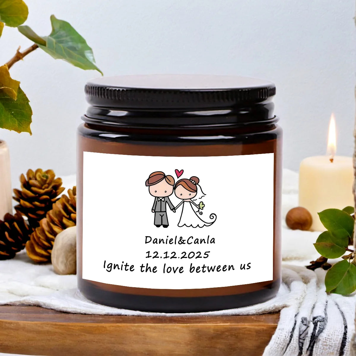 A dark glass jar candle with a white label featuring the names Daniel & Canla and the date 12.12.2025