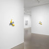 A white gallery wall featuring a yellow resin banana sculpture mounted on the wall.