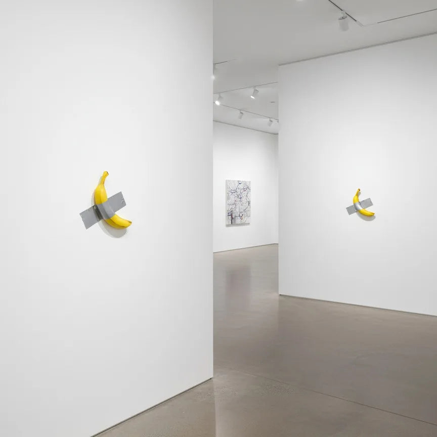 A white gallery wall featuring a yellow resin banana sculpture mounted on the wall.