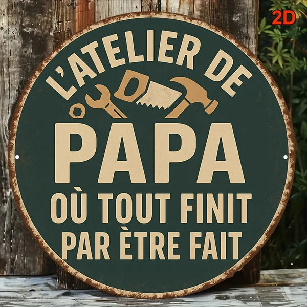 Vintage metal sign with text 'L'ATELIER DE PAPA OU TOUT FINIT PAR ÊTRE FAIT' on a dark green background