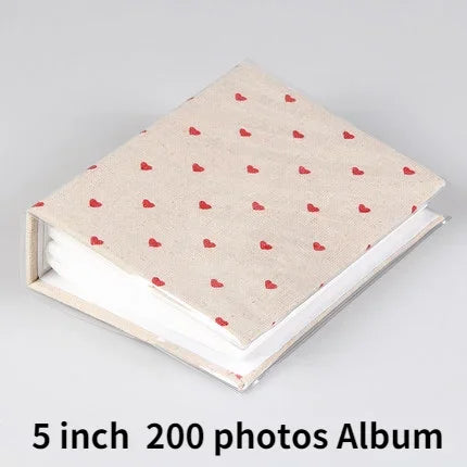 A beige photo album with a light pink patterned cover and white pages.