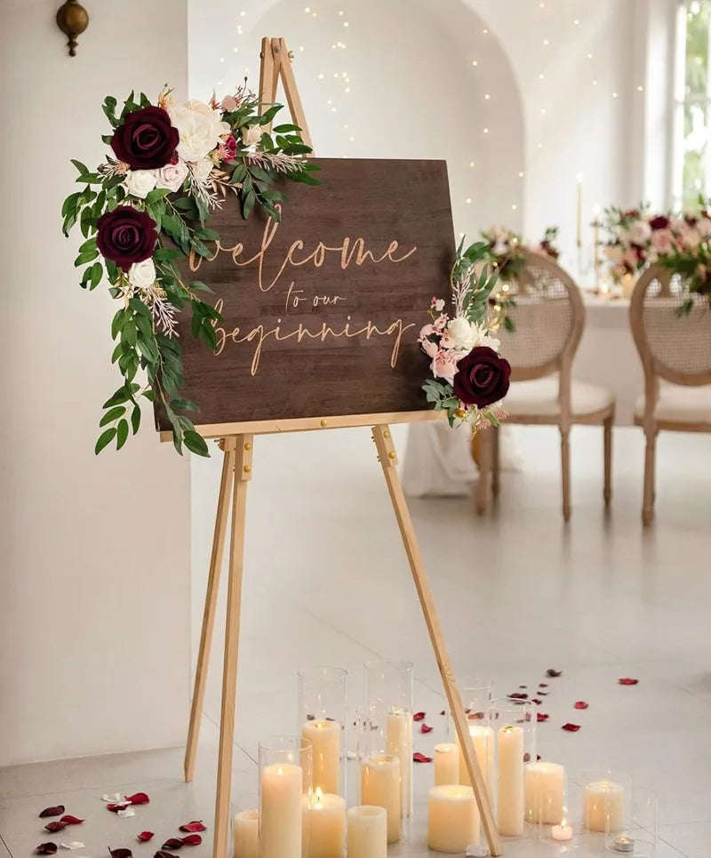 A wooden sign welcomes guests to a beginning decorated with artificial roses and greenery, set in a bright room.